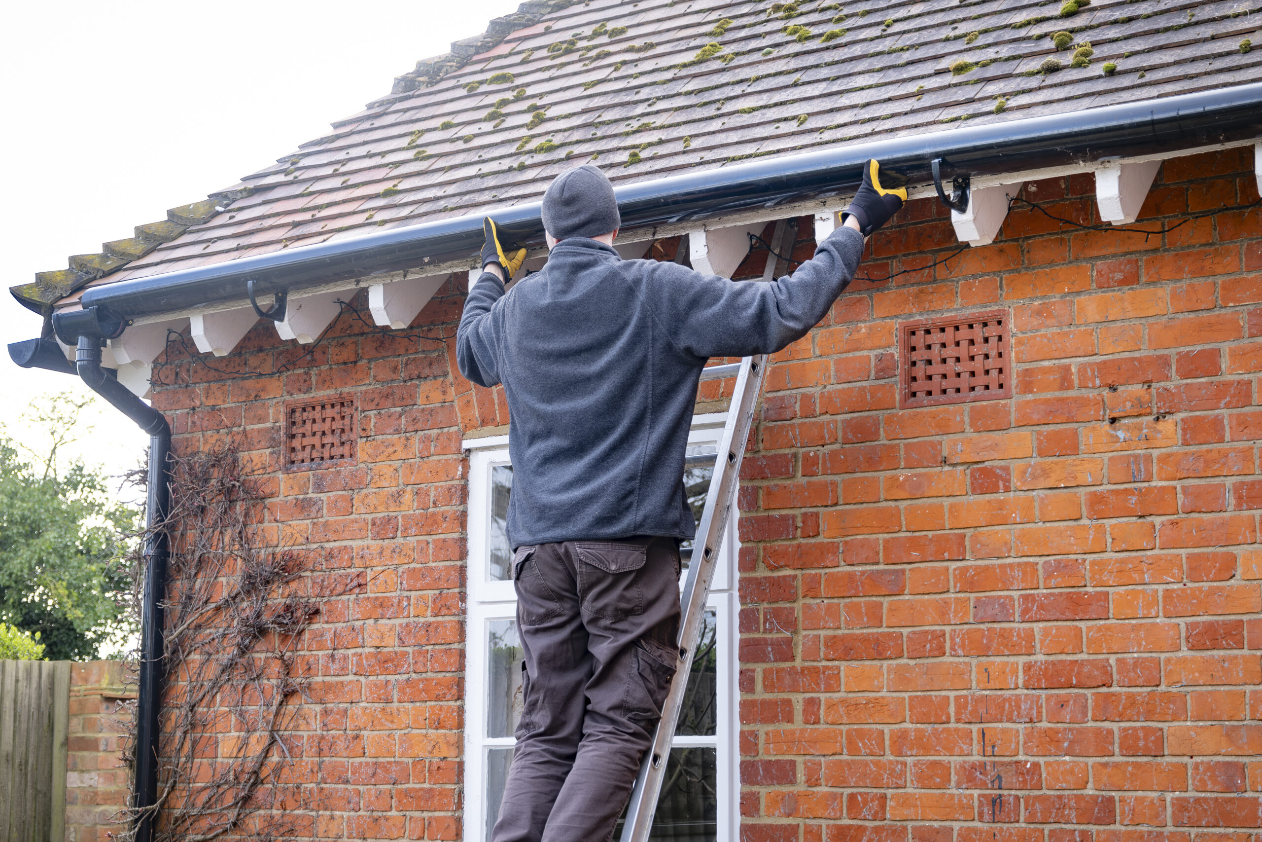 Man on a ladder fixing rain gutter on a UK house